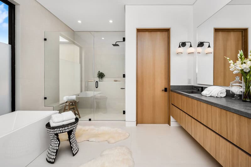 Modern bathroom renovation with glass shower, black countertop, and wood accents by Tixan Construction.