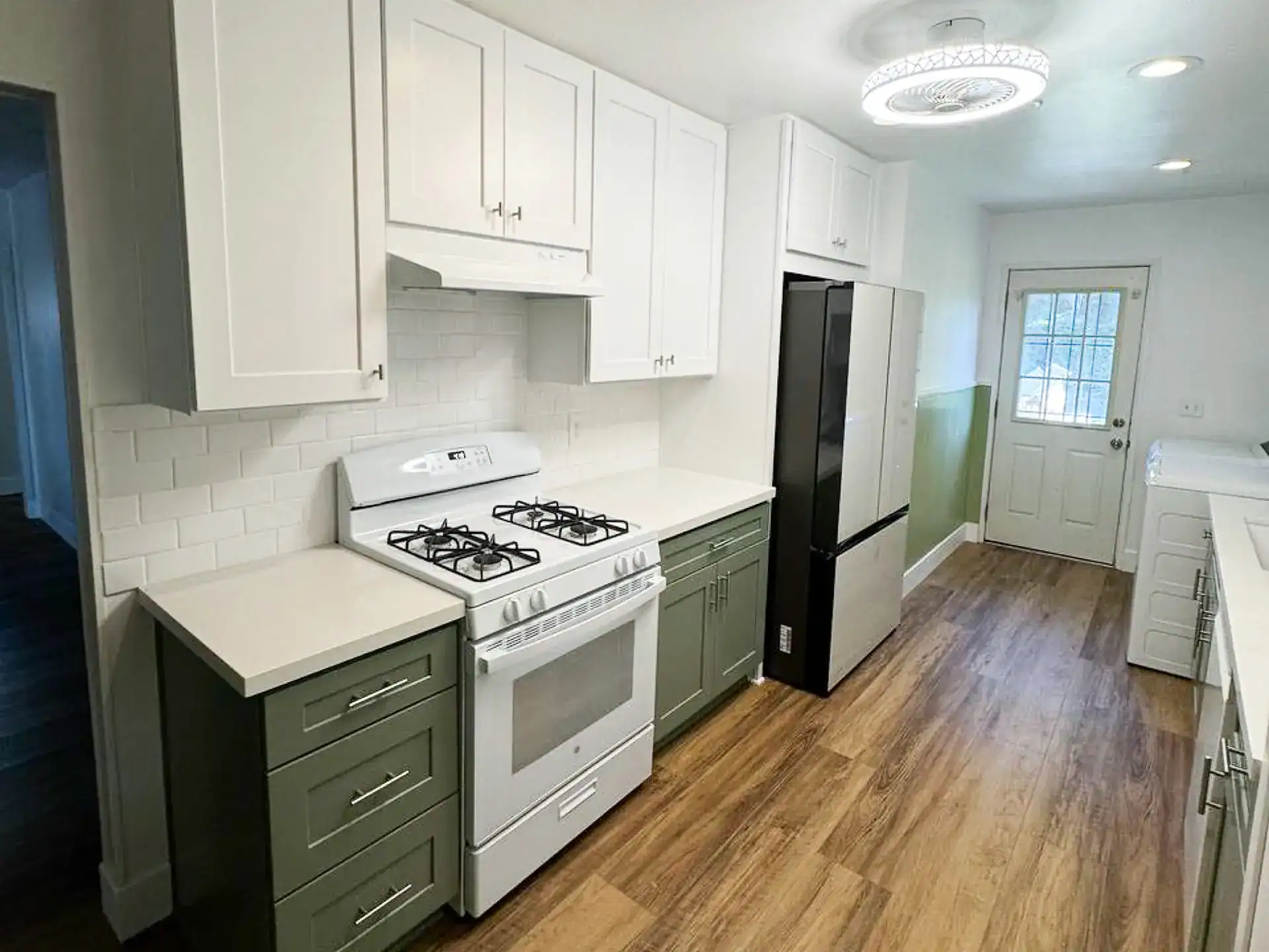 A remodeled kitchen with two-tone shaker cabinets, featuring white uppers and sage green base cabinets, with a white subway tile backsplash.
